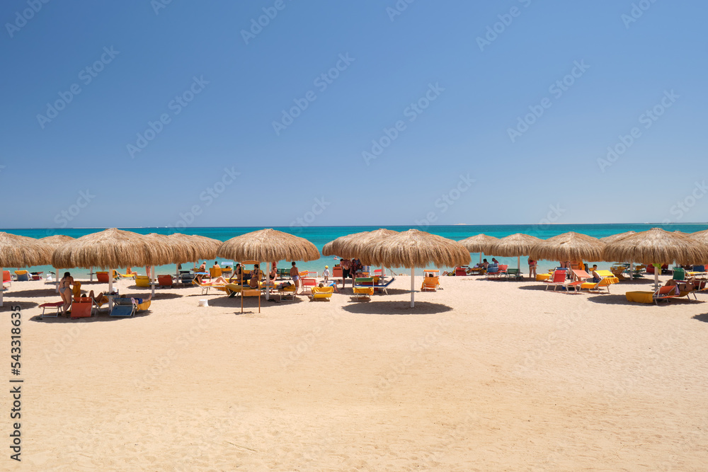 Straw shade umbrellas on sea tropical beach with resting sunbeds against blue vibrant sky in summer Straw shade umbrellas on sea tropical beach with resting sunbeds against blue vibrant sky in summer