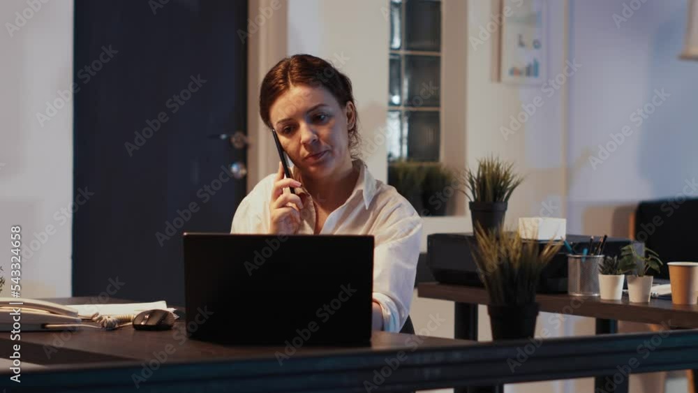 Female manager talking on phone call with smartphone late at night, using mobile phone line to chat with employee and plan business meeting. Having remote conversation to do presentation. Female manager talking on phone call with smartphone late at night, using mobile phone line to chat with employee and plan business meeting. Having remote conversation to do presentation.