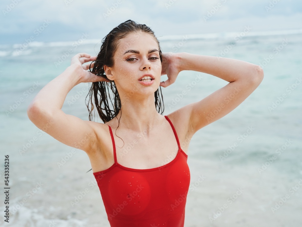 Sexy woman in red swimsuit on ocean beach with wet hair covers face ...