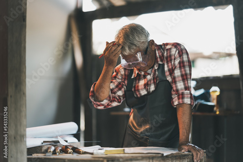 Senior carpenter use hand over head thinking or serious or sad or depression for project working on wood working machines in carpentry shop. man works in a carpentry shop.