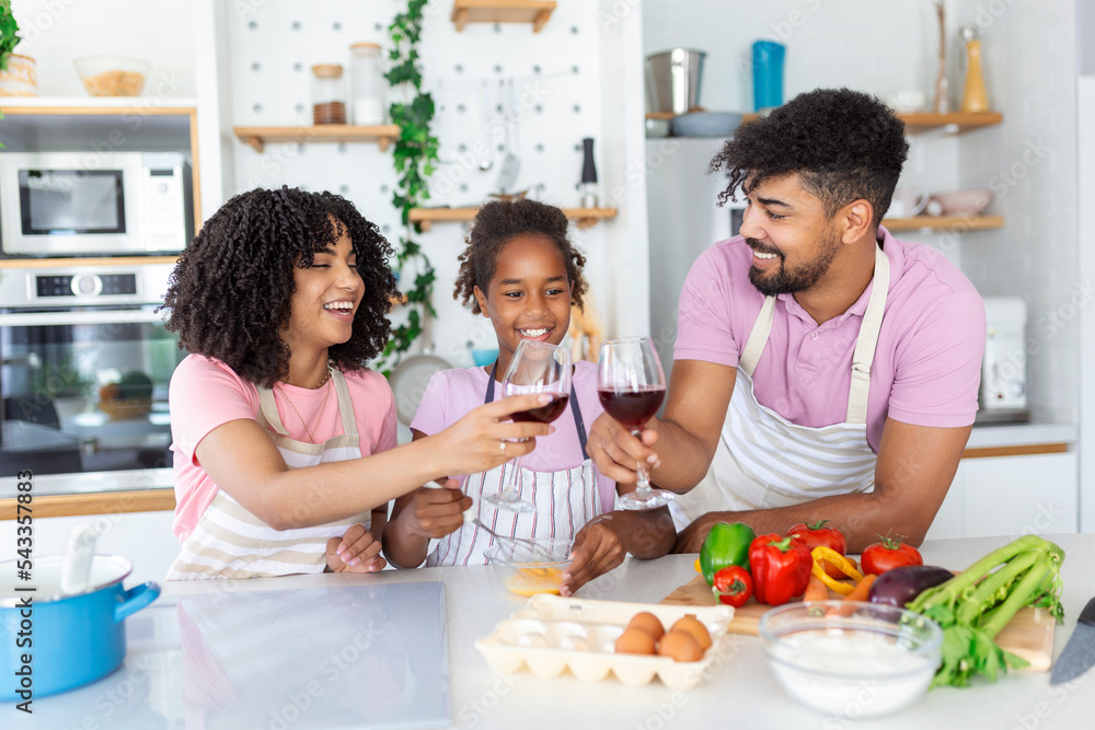 Shot of beautiful cute family having fun while cooking together in the kitchen at home. Cute little girl and her beautiful parents are smiling while cooking in kitchen at home