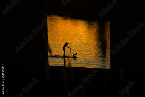 Silhouette of paddle boarder with dog at sunset