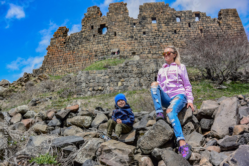 A girl with a child on the background of the 7th-century Amberd fortress, located on the slopes of mount Aragats at the confluence of the Arkashen and Amberd rivers, may 3, 2019, Armenia.