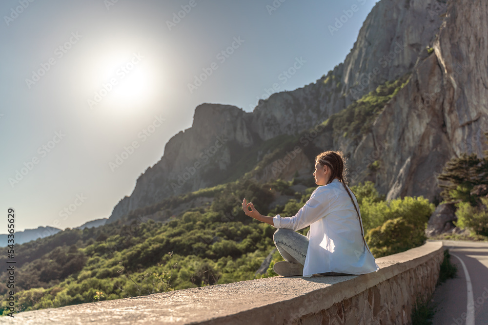 Profile of a woman doing yoga in the top of a cliff in the mountain. Woman meditates in yoga asana Padmasana