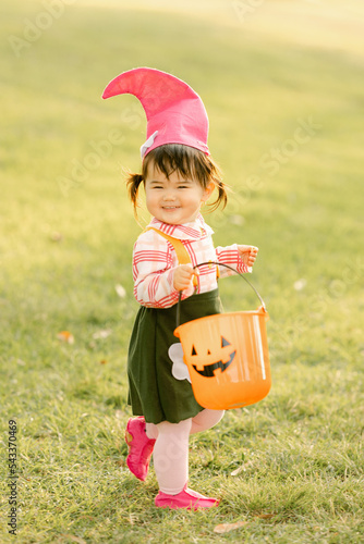 little girl wears garden gnome costume with halloween basket in the park