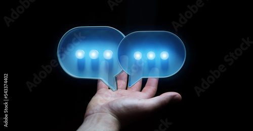 Businessman in dark using digital speech bubbles talk icons. Minimal conversation or social media messages floating over user hand. 3D rendering