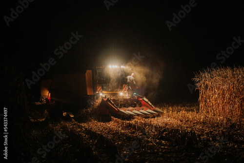Żniwa w nocy, rolnik wychodzi z kombajnu do kukurydzy