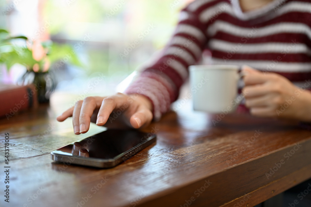 A young Asian woman sipping coffee, using her smartphone on the table