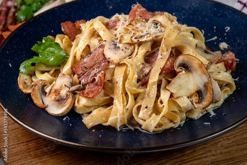 Tagliatelle in a creamy sauce with mushrooms and parmesan close-up in a blue plate.