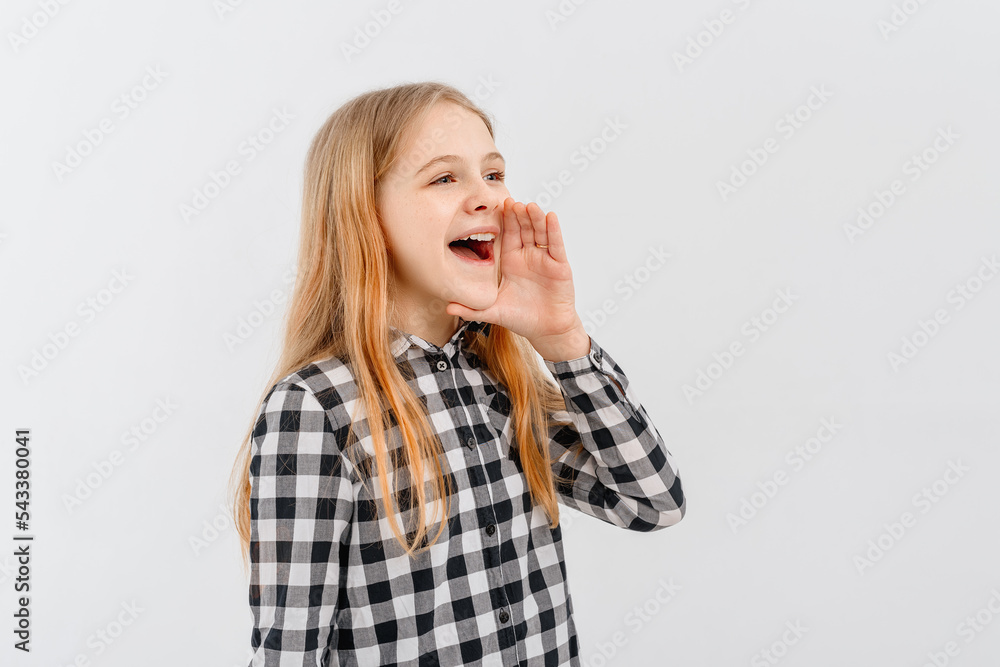 Attractive teen girl holding palm near wide open mouth is announcing, telling a secret, shouting or yelling, standing in casual plaid shirt over white background. Communication and promo concept Attractive teen girl holding palm near wide open mouth is announcing, telling a secret, shouting or yelling, standing in casual plaid shirt over white background. Communication and promo concept