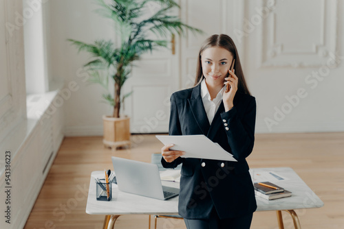 Positive young businesswoman talking on phone with copartner photo