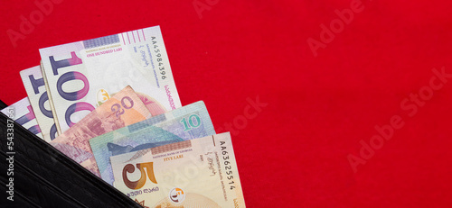 Georgian banknotes of different denominations stick out of a black leather wallet on a red textile background. 100 GEL. 20 lari. Cash paper money. Money to pay for purchases, credit, debt, mortgage