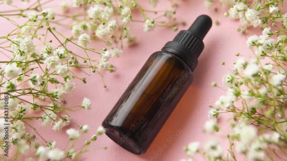 Brown glass dropper bottle with dry plants on pink background. Skincare products , natural cosmetic.