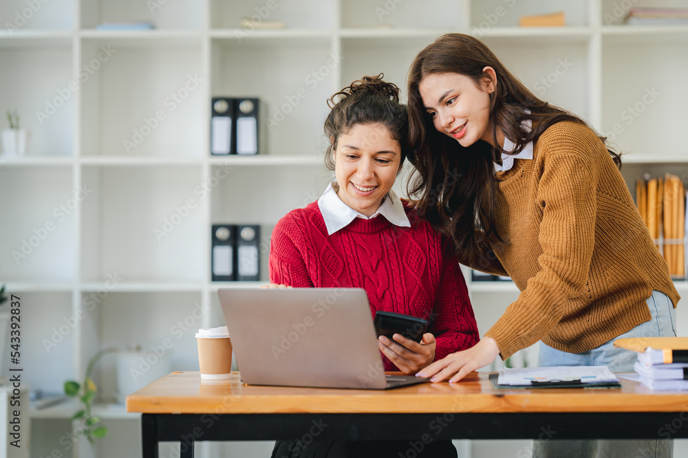 Two diverse female designers smile as they work together at a conference room table during a meeting in a modern office. collaboration concept Two diverse female designers smile as they work together at a conference room table during a meeting in a modern office. collaboration concept