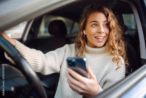 Portrait of a young woman texting on her smartphone while driving a car. Car sharing, rental service or taxi app. photo