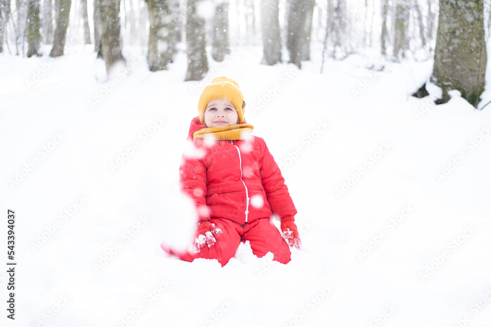 Cute little girl in pink snowsuit plays with snow in winter forest