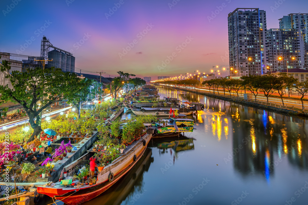 Naklejka premium Ho Chi Minh City, Vietnam - January 31st, 2022: Flowers boat at market along canal wharf. This place Farmers sell apricot blossom and other flowers on Lunar New Year in Ho Chi Minh city, Vietnam