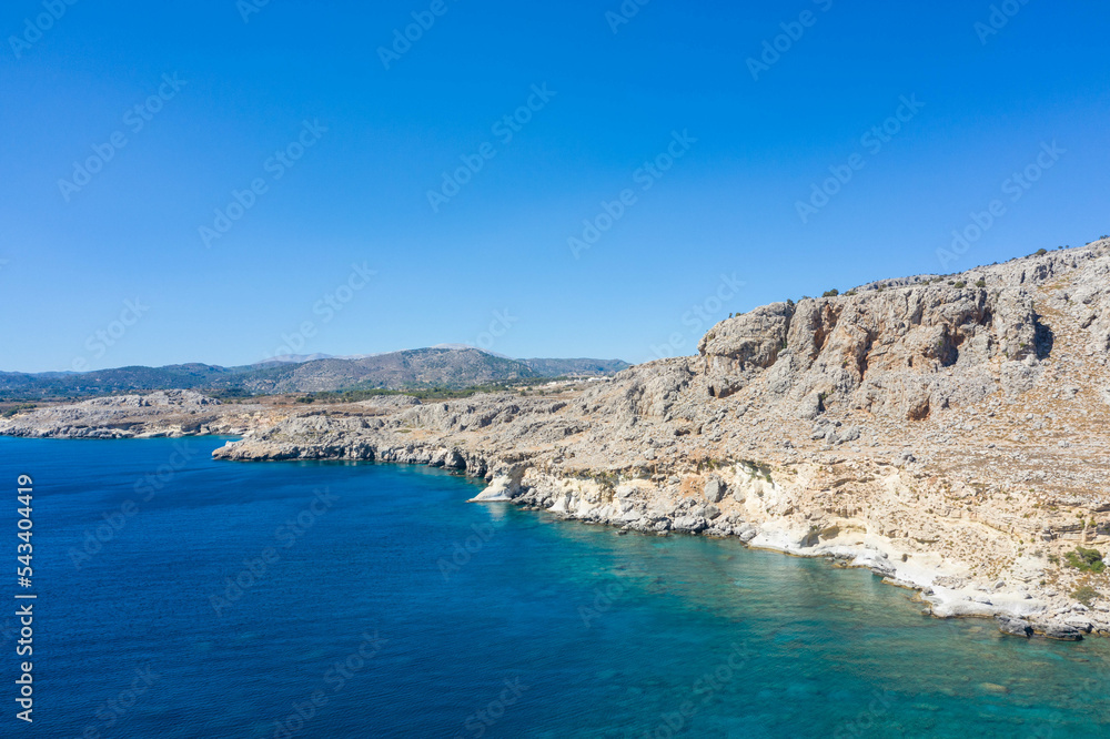 Aerial view of a peaceful rocky coastline and beautiful turquoise waters with mountain range.
Mediterranean Sea, Rhodes Island, Greece.