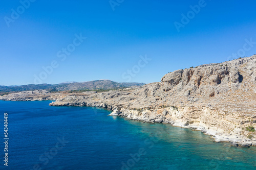 Aerial view of a peaceful rocky coastline and beautiful turquoise waters with mountain range. Mediterranean Sea, Rhodes Island, Greece.