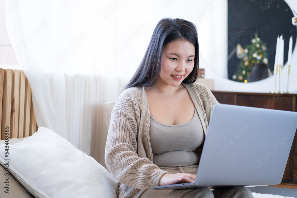 attractive young asian women in cozy clothing using laptop on bed at home, christmas time. attractive young asian women in cozy clothing using laptop on bed at home, christmas time.