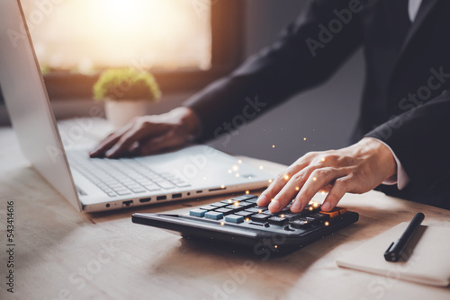 Businessman using a calculator and laptop (notebook) of Data analysis, Paperwork, financial research, and report. Individual income tax paid and corporations concept. photo