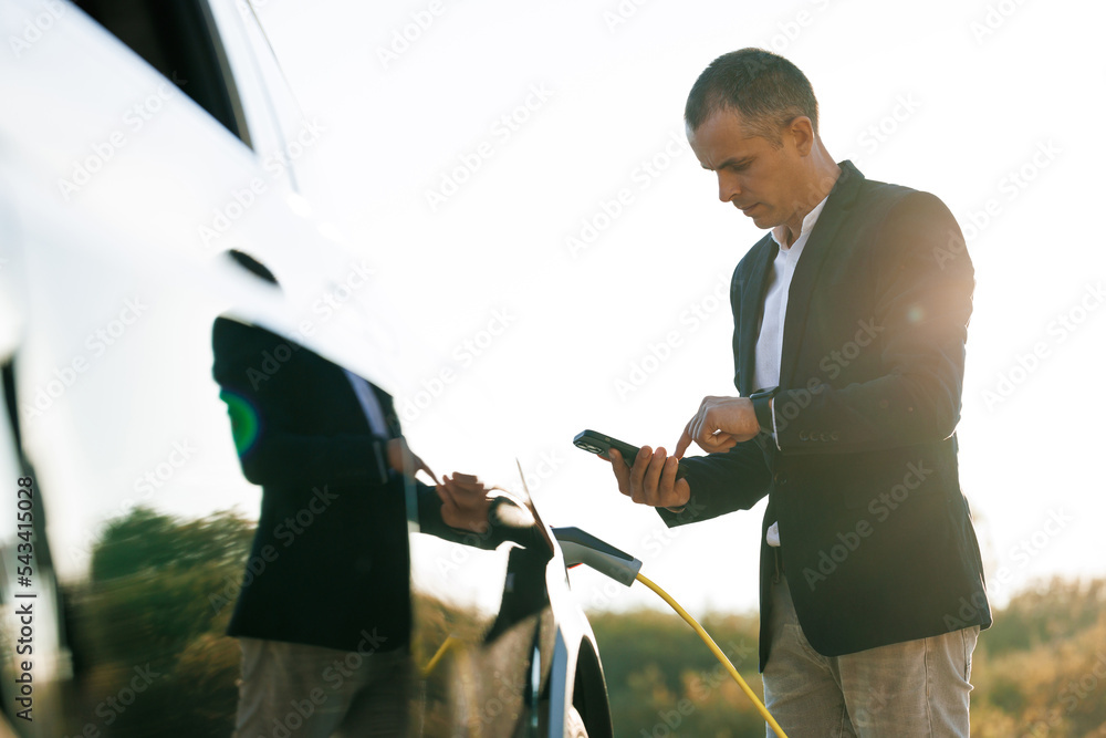 Male charging EV vehicle outdoors at sun light. Businessman unplugging