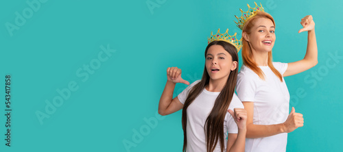 Mother and daughter child banner, copy space, isolated background. Happy woman and girl kid in crowns point fingers at promotional tshirts for copy space, advert. © Olena
