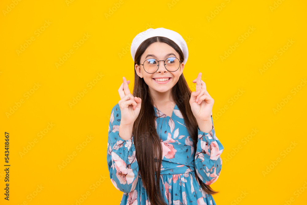 Teenager child holding fingers crossed for good luck. Teen girl prays and hopes dreams come true, isolated on yellow background. Happy teenager, positive and smiling emotions. Teenager child holding fingers crossed for good luck. Teen girl prays and hopes dreams come true, isolated on yellow background. Happy teenager, positive and smiling emotions.