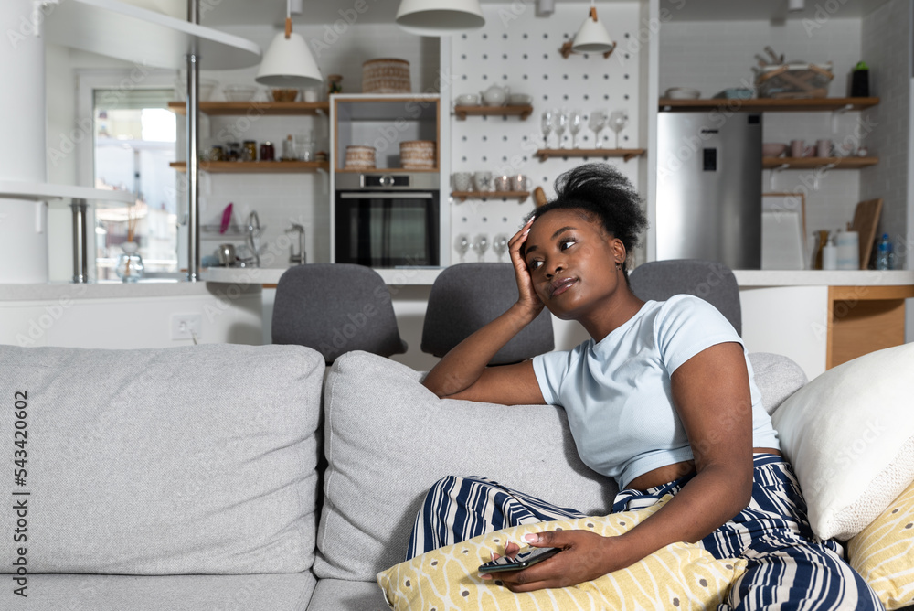 Obraz premium Depression Concept. Portrait of frustrated African American woman looking at smartphone, checking social media, lying on the couch. Upset black lady waiting for his message or call, reading bad news