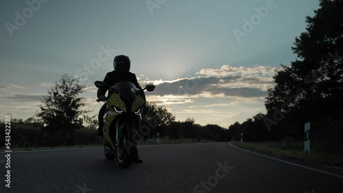 Shot of a man standing on his motorcycle in the middle of the road on a freeway in countryside during the sunset. photo