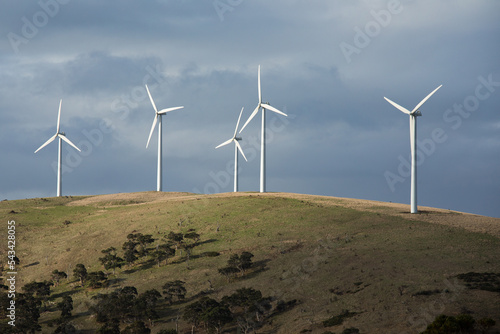 A row of wind turbines on a grassy hill in a paddock