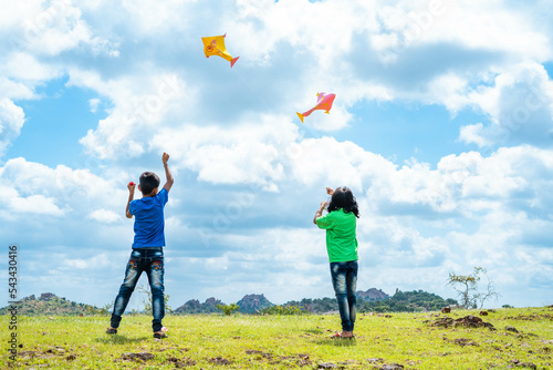 Back view shot of teenager kids flying kite on top of mountain - concept of weekend holidays, relaxation and playful childhood lifestyles.