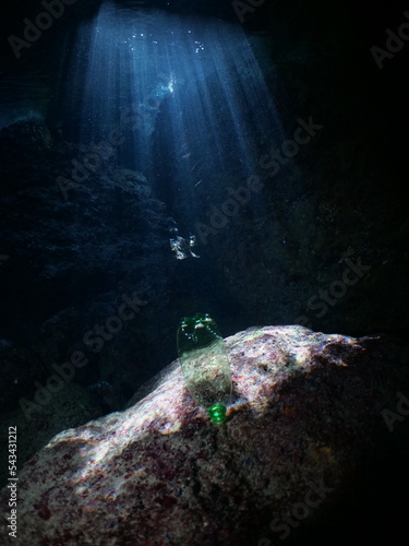 plastic bottle in a cave underwater sun beams and rays ocean pollution