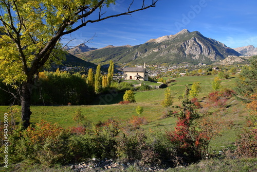 The chapel of Villard Saint Pancrace, located on a hill near Briancon, Hautes Alpes (French Southern Alps), France, surrounded by Autumn colors and with the town of Briancon in the background photo
