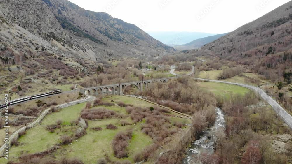 Aerial: passenger train in a valley crossing a river on ancient viaduct in the Pyrenees, southern France Aerial: passenger train in a valley crossing a river on ancient viaduct in the Pyrenees, southern France