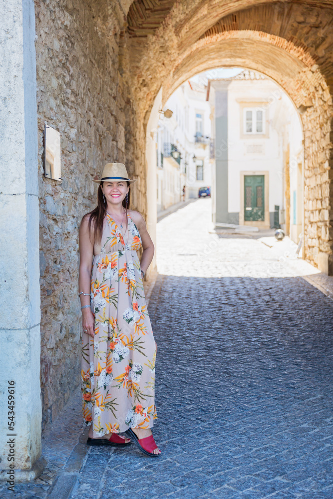 Portrait of an attractive tourist woman in old town Wearing stylish long dress, bracelets and straw hat.