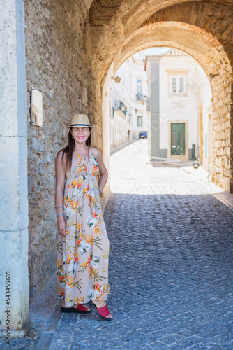 Portrait of an attractive tourist woman in old town Wearing stylish long dress, bracelets and straw hat. © svittlana