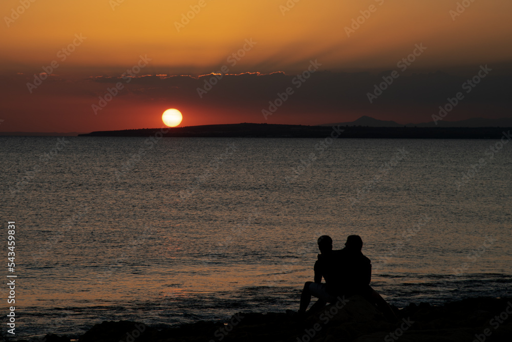 Silhouette of young couple enjoying beautiful sunset at the beach. Romantic moment human relationship