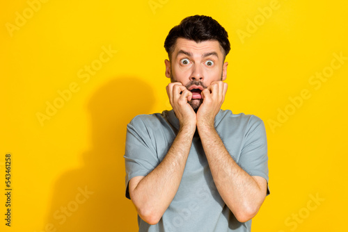 Closeup photo of young excited stressed funny man bearded bite fingers nervous scared watching movie unexpected isolated on yellow color background