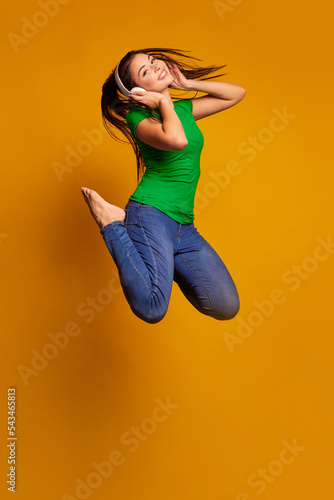 Jumping high, flying. Young woman's portrait on color studio background. Beautiful female model with headphones. Concept of human emotions, facial expression, youth, sales, ad.