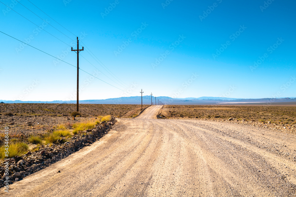 Dirt road and the blue sky in the arid wilderness field with electricity poles and cables