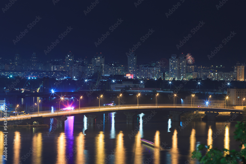 Car bridge over the river in a big city in a European city. Night landscape of a metropolis with a river, bridge and high-rise buildings.