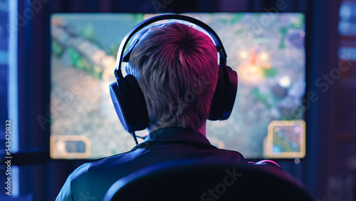 Back of the Head Angle of a Young Female Gamer Wearing Headset and Playing a Video Game on Personal Computer in a Neon Lit Living Room at Home. Cozy Evening for a Pro PLayer at Home in Loft Apartment.