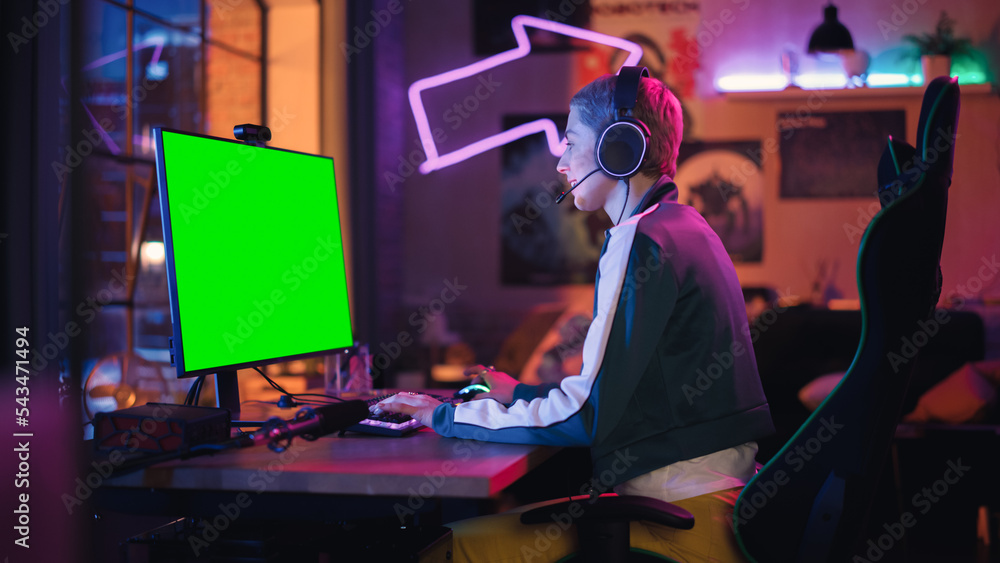 Attractive Female Gamer Playing Online Video Game with a Mock Up Green Screen on Her Powerful Computer. Room and PC have Colorful Neon Led Lights. Cozy Evening at Home in Loft Apartment.