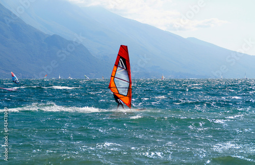 a surfer windsurfing on the turquoise waves of lake Garda by the mediterranean town Riva del Garda with the Italian Alps in the background , Lombardy, Northern Italy