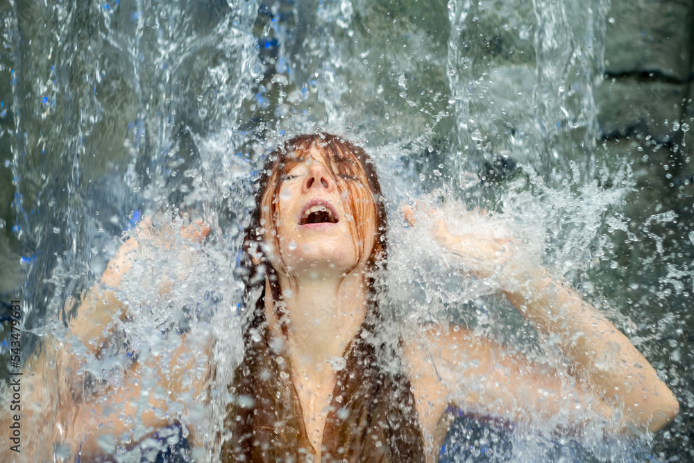 Fototapeta premium beautiful young cute sexy redhead woman with open mouth, enjoying the splashing water of the waterfall in the Spa Wellness feels the falling water