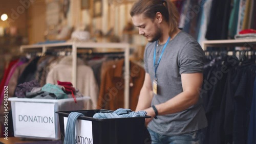 Male volunteer sort donated clothes in second-hand store. Realtime