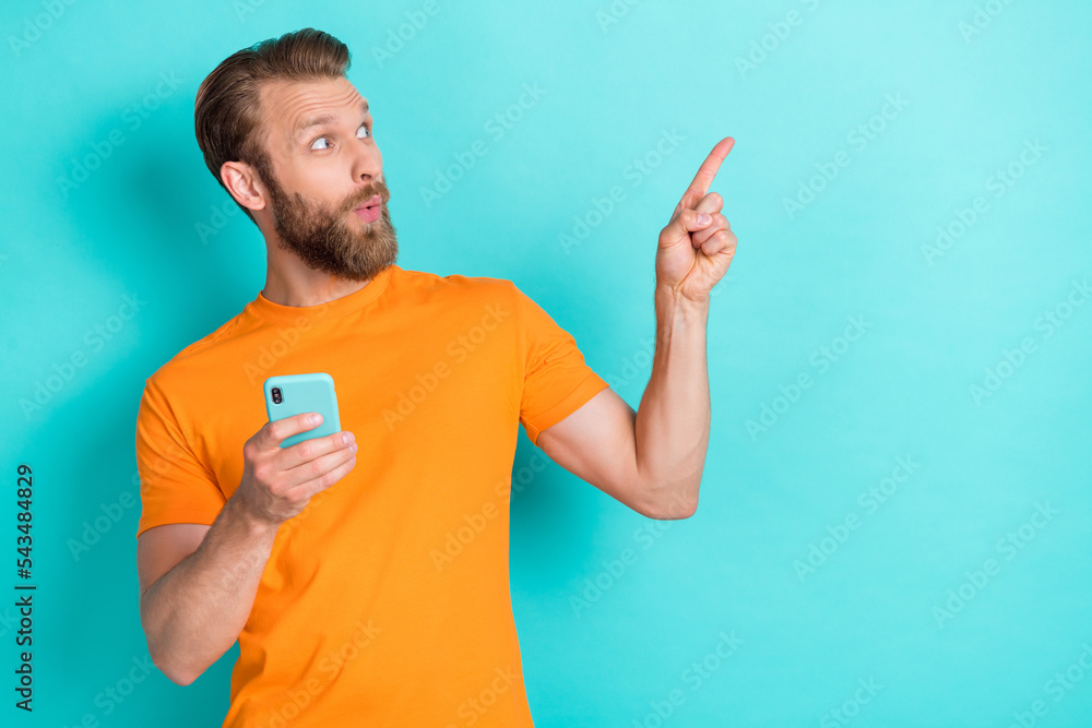 Portrait of impressed man look direct finger empty space hold telephone isolated on teal color background Portrait of impressed man look direct finger empty space hold telephone isolated on teal color background