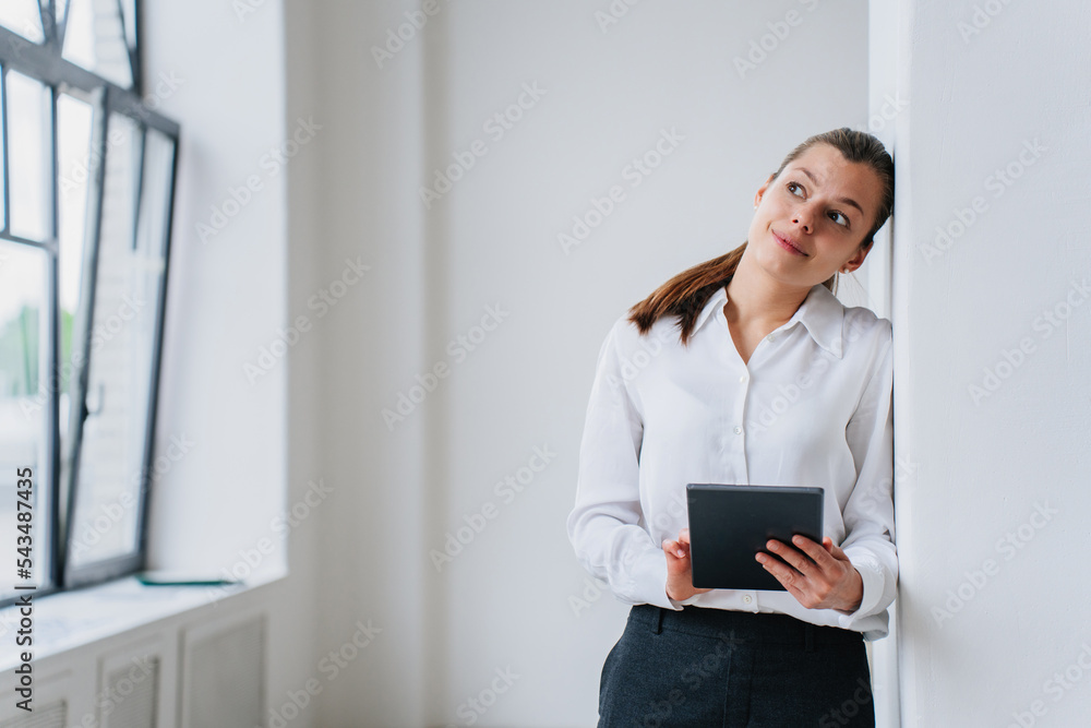 Dreamy student girl thinks about future, career, standing indoor, leans on wall looks aside holds tablet. Attractive thoughtful hispanic woman designer stands against empty interior. Successful people Dreamy student girl thinks about future, career, standing indoor, leans on wall looks aside holds tablet. Attractive thoughtful hispanic woman designer stands against empty interior. Successful people