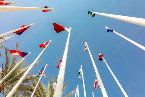 Flags of different countries of world flutters in wind background of blue sky. Bottom up view. High quality photo